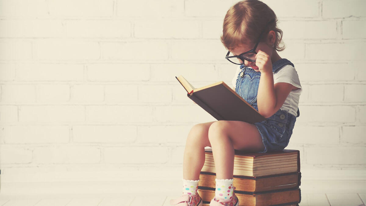 Criança sentada em cima de alguns livros praticando uma Leitura Criativa.