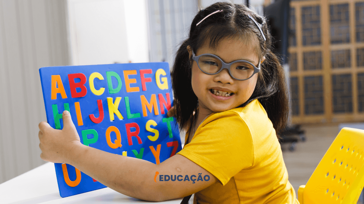 Educação especial - menina com Síndrome de Down segurando uma placa com o alfabeto