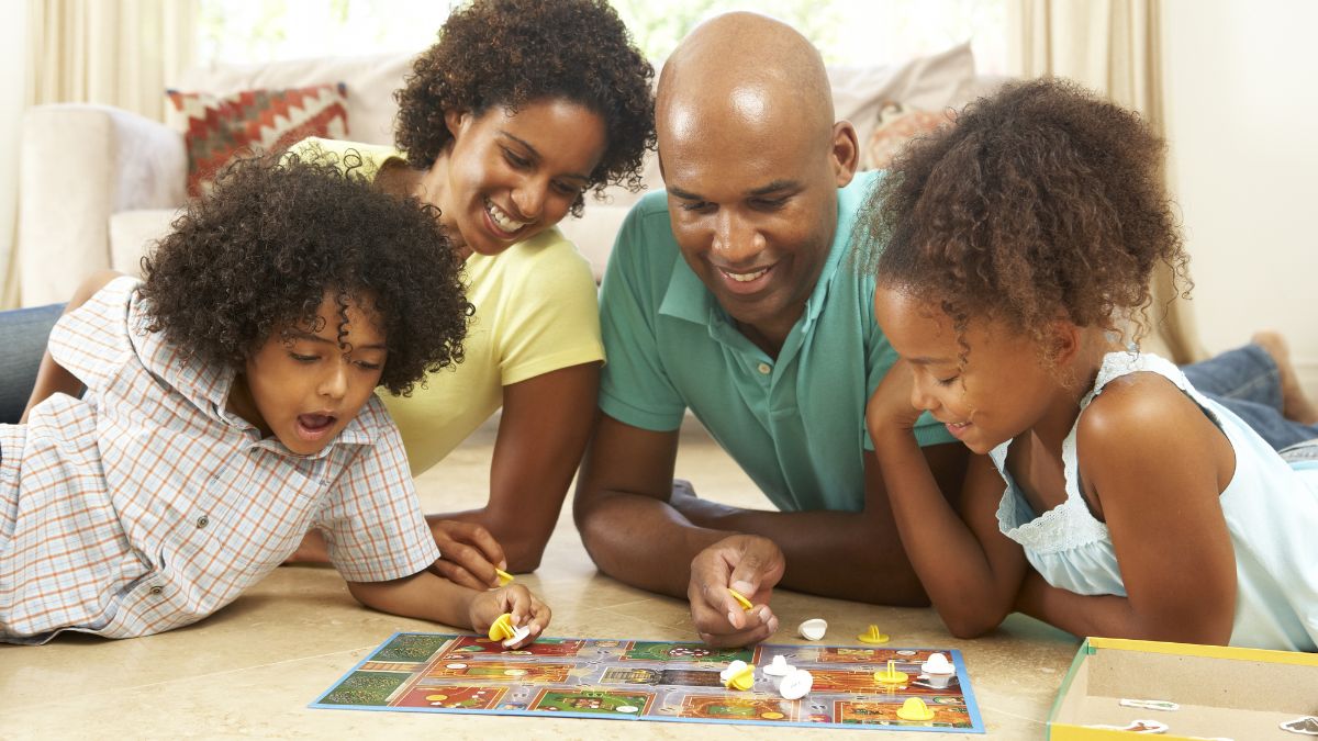 Pais e filhos brincando de jogo de tabuleiro. Imagem: Canva Pro