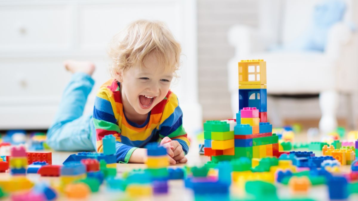 Criança de aproximadamente de 3 anos de idade, montando blocos colorido e muito contente. 
Imagem: FamVeld de Getty